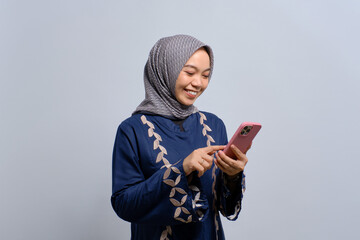 Smiling young Asian Muslim woman using mobile phone, getting good news isolated on white background