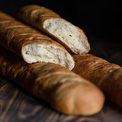 Freshly baked wheat flour baguettes. Two baguettes on wooden surface in cut form. French pastries. White bread. Dark background. Close-up. Side view. Soft focus. Copy space. 