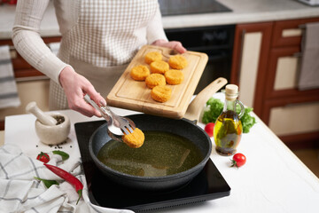 Woman puts cheese balls into frying pan with hot cooking oil