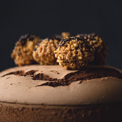 Candies made from dried fruits and nuts on surface of chocolate cake. Chocolate brownie. Nut balls. Decor for baking. Close-up. Dark background. Soft focus. 