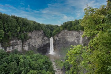 Obraz premium Taughannock Falls on a sunny day, surrounded by rock faces and trees, the watercourse emptying into a pool.