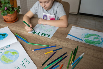 A child at home at the table draws the planet Earth with a world map with multi-colored pencils and...