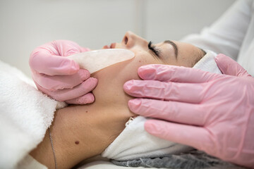 Obraz na płótnie Canvas Young pretty woman receive facial massage with guasha treatment at beauty clinic