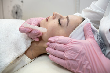 Fototapeta na wymiar Young pretty woman receive facial massage with guasha treatment at beauty clinic