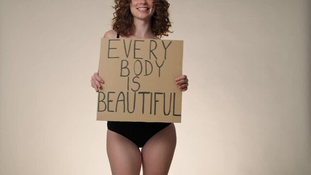 Cheerful caucasian red head woman in underwear in the studio holding a banner. Shot with RED helium camera in 8K. 
