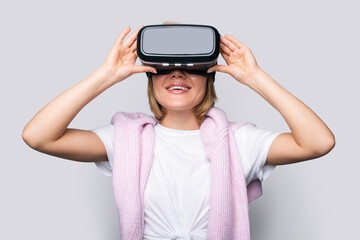 Front view portrait of a young woman touching VR goggles while exploring virtual reality isolated against white background. Virtual reality, digital technology