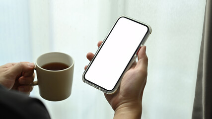 Hand holding cup of coffee and smart phone with white blank display, empty screen for graphic display montage