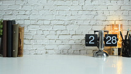 Creative workplace with a vintage flip clock, pencil holder and books on white table against brick wall. Copy space for your text