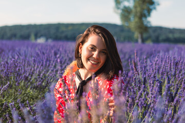 a young woman sits in a lavender field with a straw hat hanging around her neck