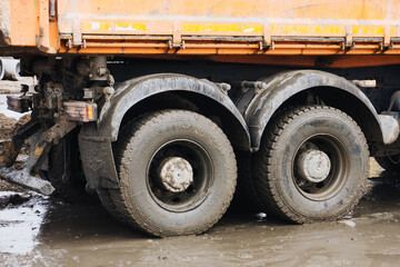 Tipper truck driving construction site. Muddy ground rainy day. Heavy vehicle. Dumper lorry. Big rubber tyres.	