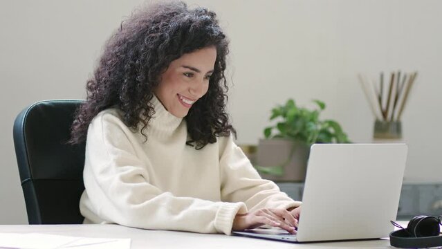 Happy young latin professional business woman looking at laptop reading good news on email feeling excited by new job offer, salary growth, winning online, satisfied by great online work results.