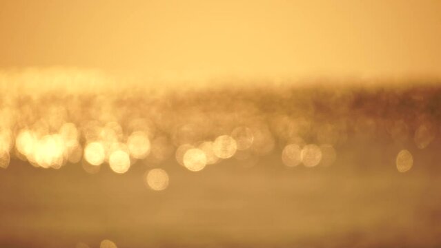 Blurred golden sea at sunset. The sun reflects and sparkles on the waves with bokeh, illuminating the golden sea. Holiday recreation concept. Abstract nautical summer ocean sunset nature background.