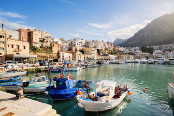 View of Castellammare del Golfo town, Sicily island, Italy. Beautiful mediterranean port with fishing boats over old town background. Popular travel destination in Europe - obrazy, fototapety, plakaty