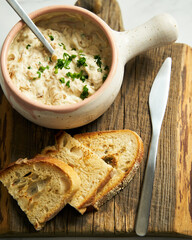 Sour cream, yogurt and caramelized onion spread dip in the bowl on wood board bread pieces are near spreader with dip