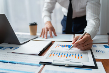 Young Asian businessmen sit analyzing data at the desk and pointing at charts and graphs comparing...