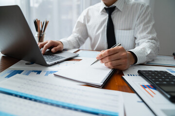 Young Asian businessman sitting analyzing financial data Management on the laptop at an office desk.