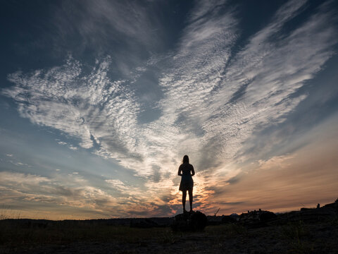 Silhouette of woman standing on rock and admiring sunset at Blake Island State Park, Washington, USA