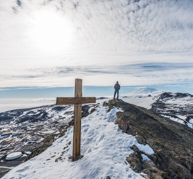 A man stand on top of Observation Hill above McMurdo Station, with the memorial to Robert Falcon Scott in the foreground.