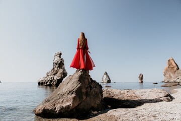 Woman travel sea. Young Happy woman in a long red dress posing on a beach near the sea on background of volcanic rocks, like in Iceland, sharing travel adventure journey