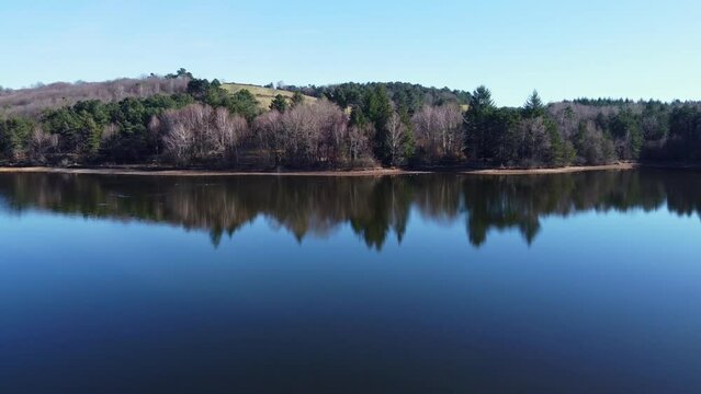 Survol d'un lac bleut&eacute; aux reflets importants et bord&eacute; par une vaste for&ecirc;t.