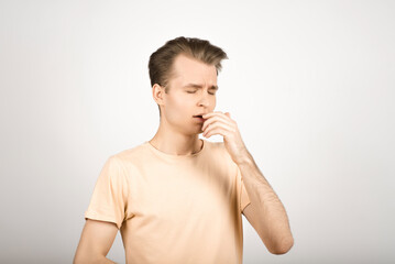 A young blond guy has an allergy and he sneezes on a white background.