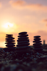 Obraz premium Vertical İmage, Balanced pebble pyramid silhouette on the beach at sunset. Zen stones on the sea beach, meditation, spa, harmony, calmness, balance concept. 