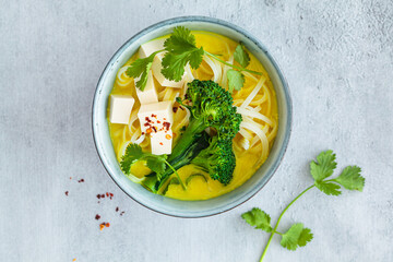 Vegan laksa with rice noodles, broccoli and tofu in blue bowls, gray background.