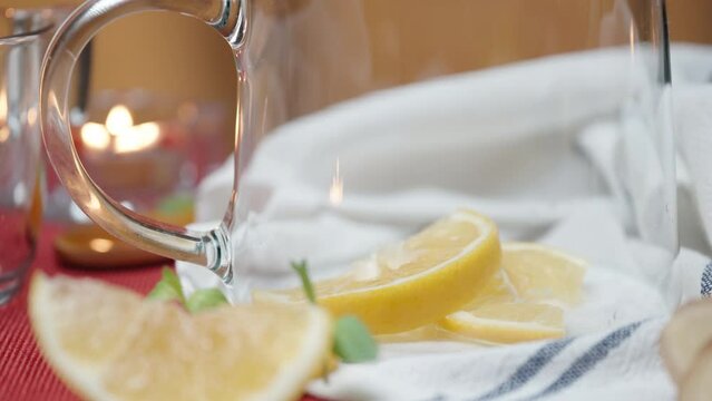I put lemon slices in a glass teapot, a candle is burning in the background, close-up.