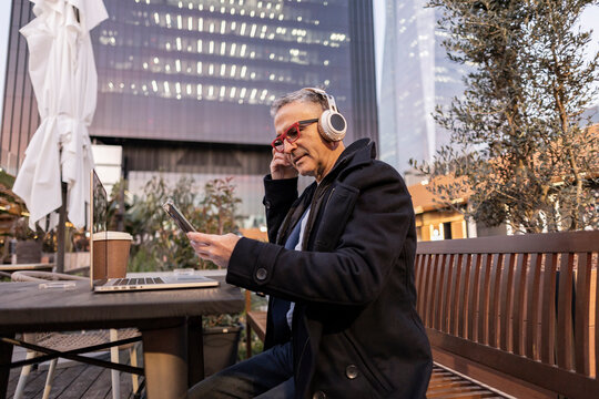 Businessman wearing wireless headphones using smart phone at table