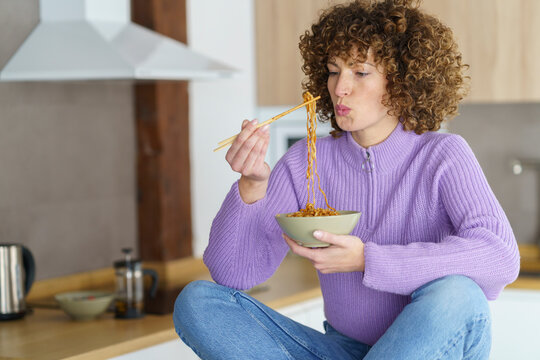 Woman with chopsticks eating noodles at home