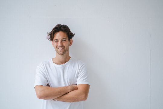 Smiling man standing with arms crossed in front of white wall