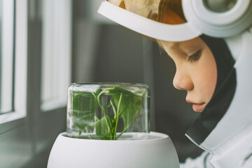 Boy wearing space suit looking at plant in glass jar