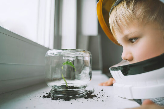Boy wearing space helmet looking at plant in glass jar