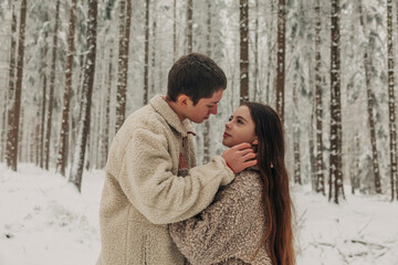 Romantic teenage couple standing together in snowy forest