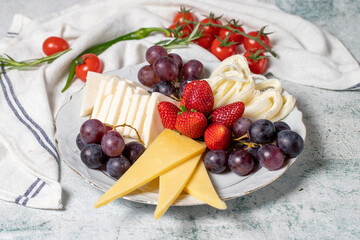 Cold cheese plate, cheese set platter. Strawberry, grape and cheese assortment on gray background