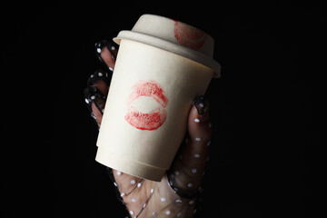 Female hand holds paper cup with kiss on black background