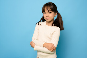 Photo of attractive little girl look empty space folded arms wear sweater isolated on blue color background