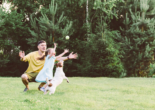 Father playing with daughter and family pet dog at backyard lawn on sunny summer day