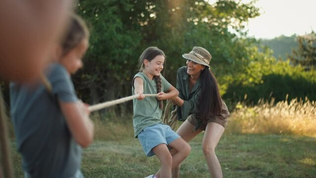 Young family with happy kids having fun together outdoors pulling rope in summer nature.