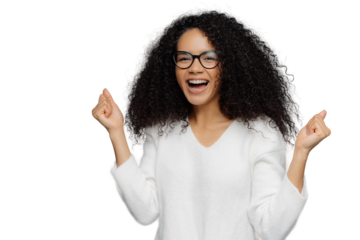 Overjoyed African American woman clenches fists with triumph, laughs with happiness, rejoices success, wears spectacles, white sweater, cheers for favourite team, isolated on grey background
