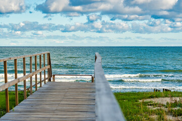 An empty wooden path with handrails for descending to a sandy beach. View of the calm sea and...