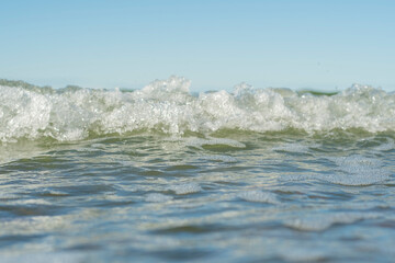 Close-up of the sea wave with the foam surging on the shore. View of sea water in soft focus. Background in a light blur on the theme of a serene summer vacation and relaxed vacation.