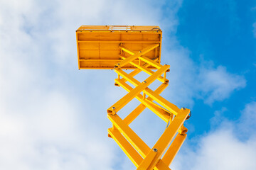 Yellow scissor lift from bottom view with blue skies in a sunny day outside 