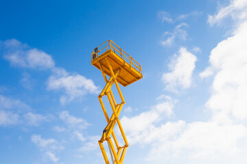 Lifted yellow scissor lift platform on blue sky background - obrazy, fototapety, plakaty
