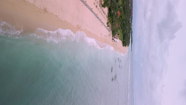 Vertical drone shot of waves rooling from the clear blue sea on Geger beach in Bali