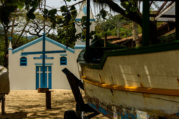 Fishing boat stored in the shade in front of the beach church in Ilhabela