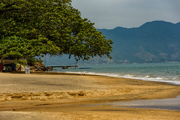 Extension of yellow sand cut by a river on a deserted beach surrounded by mountains and trees, Ilhabela, São Paulo