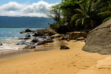 Cozy, shaded corner on a deserted beach in Ilhabela, São Paulo with rocks and vegetation, overlooking the blue sea