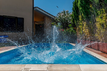 A huge splash of water is created by a cannonball dive into a swimming pool on a sunny day