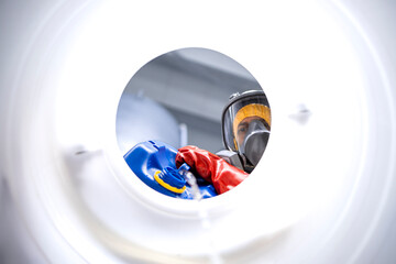 Inside barrel view of factory worker with gas mask and gloves mixing chemicals inside production...
